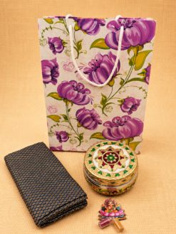 Floral paper gift bag with Meenakari decorative box, brocade blouse piece, and Lakshmi haldi kumkum set for traditional return gifts.